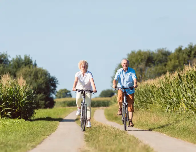 Full length of a senior active couple smiling and looking forward with confidence and serenity while riding bicycles in the countryside in summer